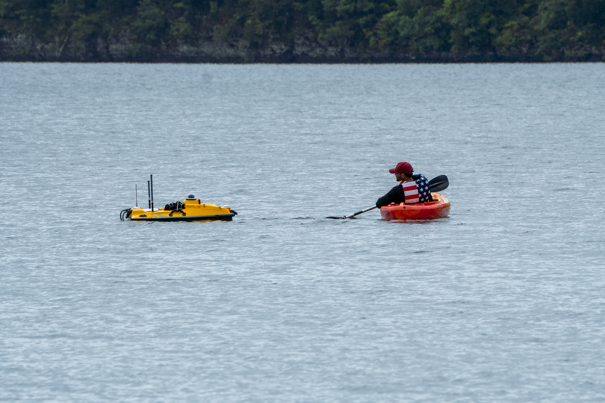 Photograph of a person in a kayak inspecting a remotely operated water vehicle.